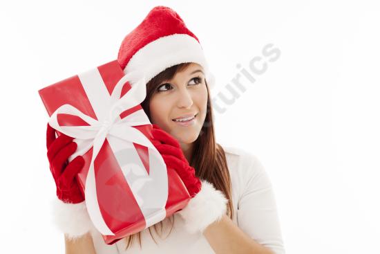 Festive young woman shaking a Christmas gift, capturing a cheerful holiday moment perfect for seasonal designs and promotions.