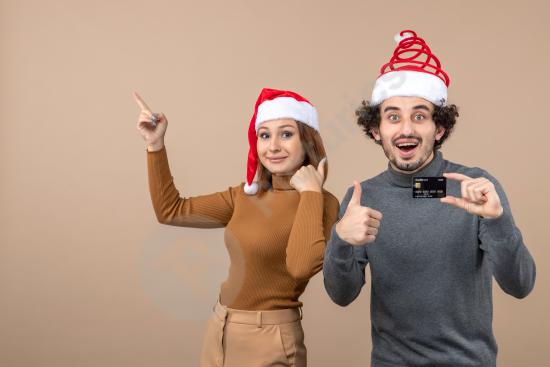 Excited couple in Santa hats celebrating Christmas shopping, showing a credit card and approval gesture, ideal for holiday sales and promotions.