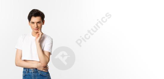 Portrait of a young queer man smiling at the camera, having an idea, standing on a white studio background. Great for creativity, identity, and inspir...