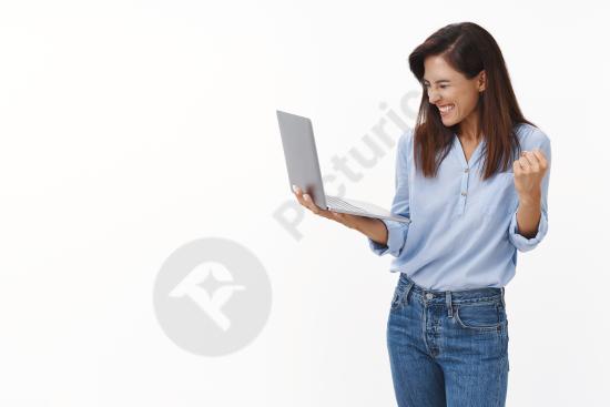 Cheerful female entrepreneur celebrating success while holding a laptop, expressing victory, motivation, and positive business results.