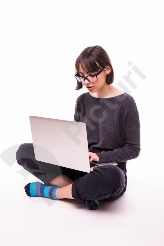 Young teen girl sitting on the floor using a laptop computer, representing online education, learning, school, and digital technology.