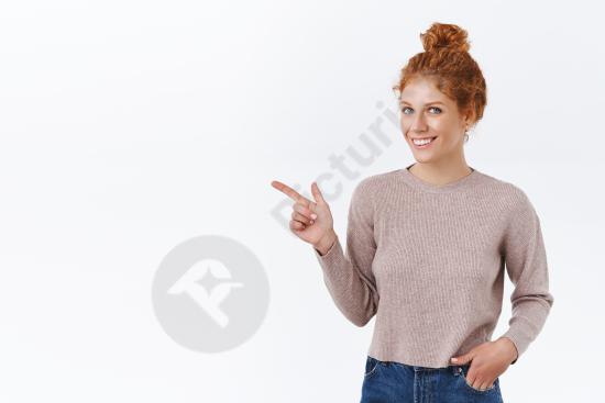 Attractive redhead woman with curly hair in a messy bun, smiling and pointing left, isolated on white background, ideal for ads and promotions.