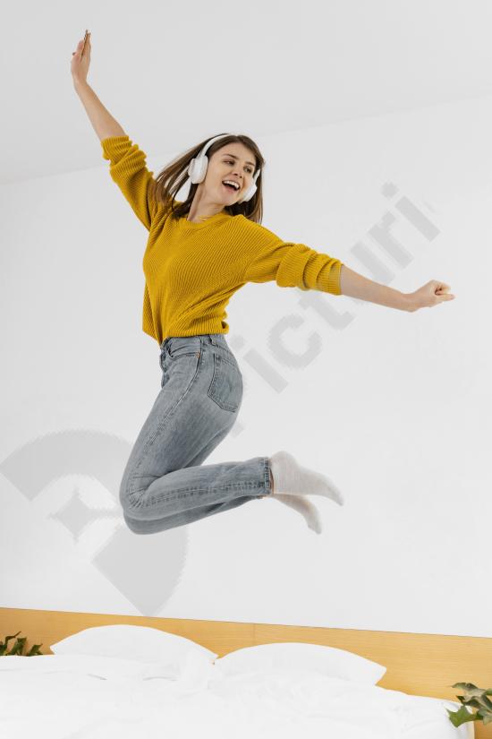 Full shot of a woman jumping while wearing headphones, expressing freedom and enjoyment of music, ideal for lifestyle, fitness, and youth content.