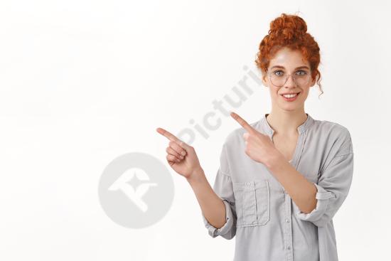 Smiling redhead European woman with curly hair in a bun pointing left at blank copy space, ideal for product promotion and advertising concepts.