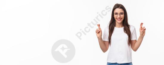Waist up portrait of an optimistic girl wearing glasses and a t shirt, crossing fingers and believing dreams come true, isolated on white background.