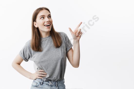 Close up of a smiling young female student pointing at copy space, looking aside with a happy expression, perfect for advertising and promotion concep...