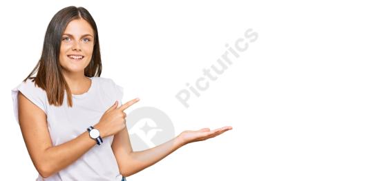 Young Caucasian woman in a casual white t shirt looking amazed and smiling at the camera while presenting and pointing with her finger.