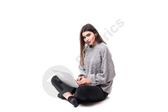 Interested brunette woman wearing a gray sweater, sitting on the floor while studying or working on a laptop in a casual indoor setting.