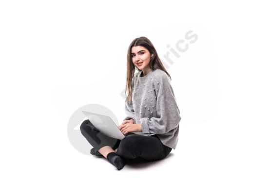 Smiling brunette woman wearing a gray sweater, sitting on the floor while studying or working on a laptop in a relaxed indoor setting.