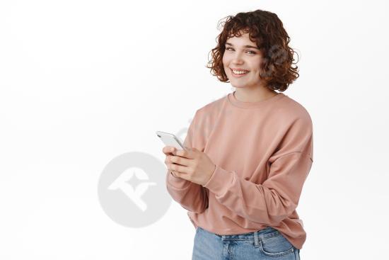 Happy woman smiling while texting a message on her smartphone, standing on a white background, representing mobile apps, chat, and modern communicatio...
