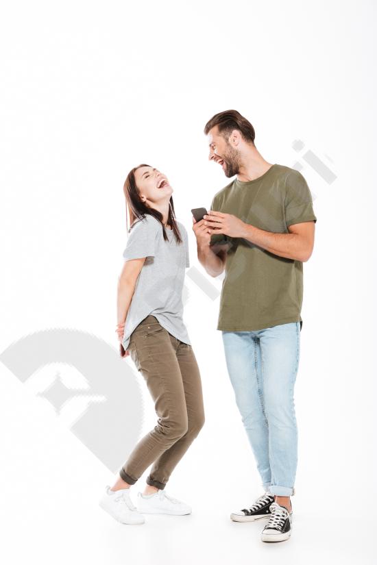 Laughing young couple holding mobile phones together, expressing love, happiness, and modern communication in a casual lifestyle setting.