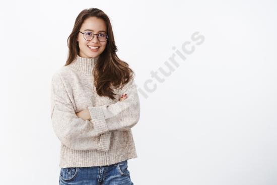 Studio shot of a stylish young woman wearing glasses and a warm sweater, smiling confidently with arms crossed in an upbeat, creative lifestyle pose.