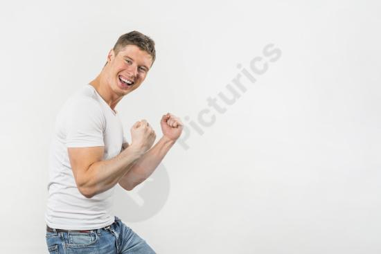 Excited young man clenching his fist in celebration against a white background, expressing success, motivation, victory, and positive emotion.