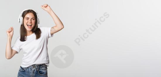 Attractive joyful girl dancing while listening to music with wireless headphones, expressing freedom, happiness, and positive lifestyle energy.