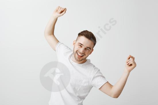 Handsome happy young man dancing in a white t-shirt against a gray wall, expressing joy, energy, and a relaxed modern lifestyle concept.