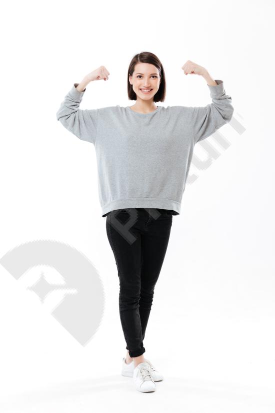 Full-length portrait of a happy woman showing her biceps, expressing strength, confidence, and fitness motivation, isolated on a white background.