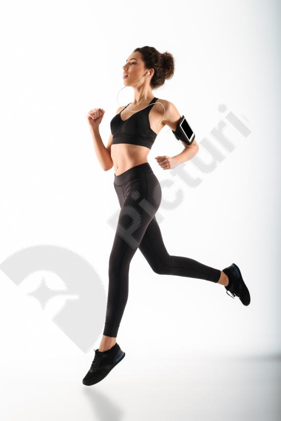 Young curly brunette fitness woman running while listening to music with headphones, enjoying workout and active healthy lifestyle.