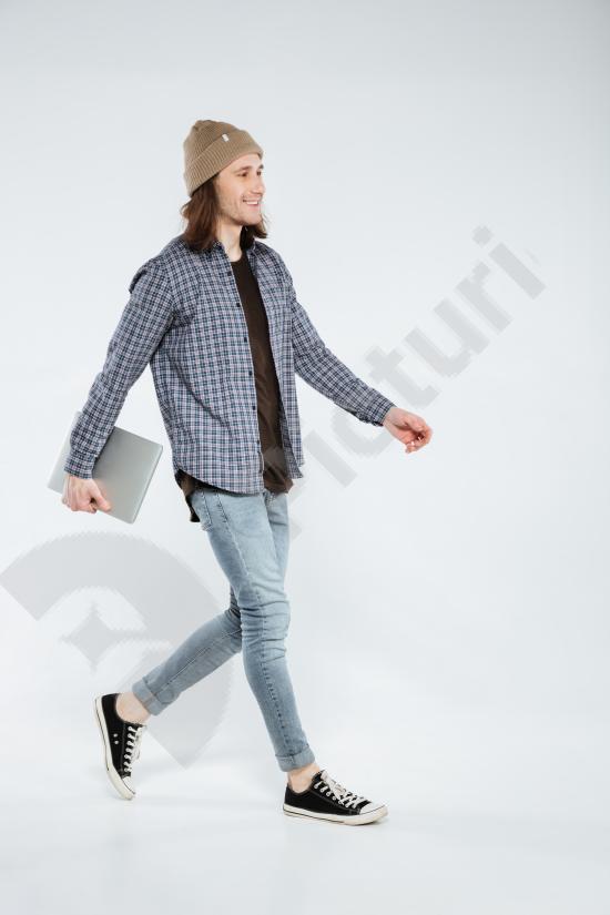 Stylish hipster walking with a laptop, modern lifestyle and technology concept. Casual urban look with confident movement and mobility.