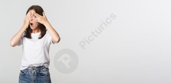 Curious beautiful girl smiling with eyes closed and peeking through her fingers. Playful portrait perfect for surprise, anticipation, and fun concepts...