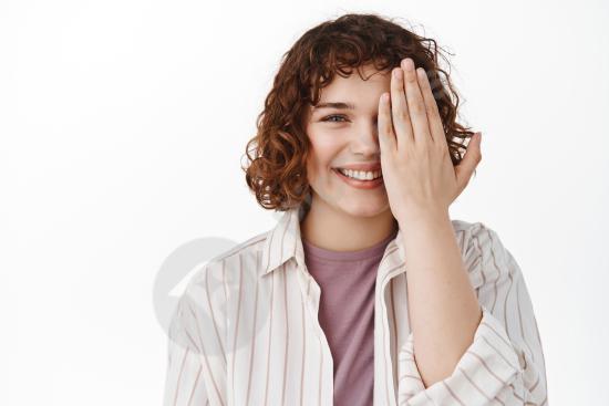 Happy woman covering one eye with her palm as if checking vision. Studio portrait perfect for optician, eyesight testing, and eye health concepts.